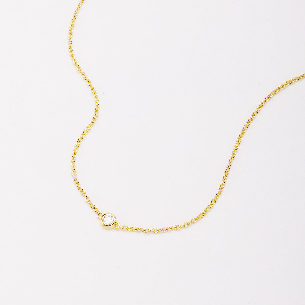 Close-up of a round bezel-set stone on a fine gold-tone chain bracelet.