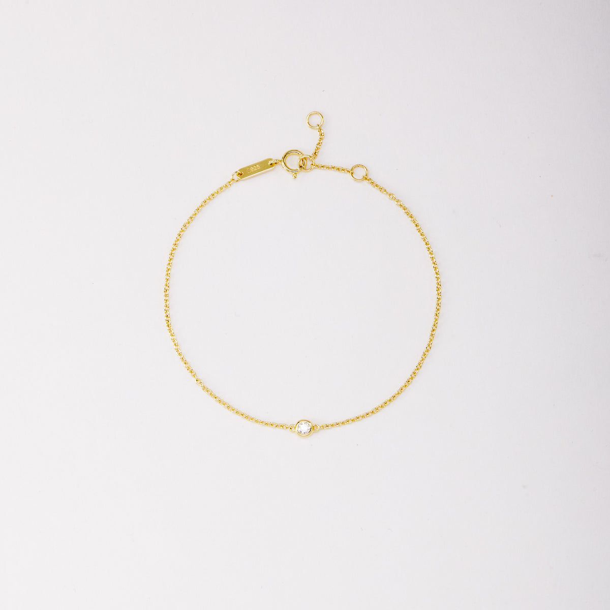 Gold-tone solitaire bracelet with a round bezel-set stone, shown laid flat on a light background. Main image