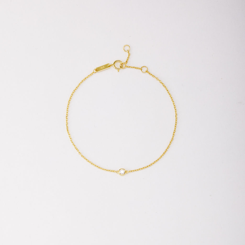 Gold-tone solitaire bracelet with a round bezel-set stone, shown laid flat on a light background.