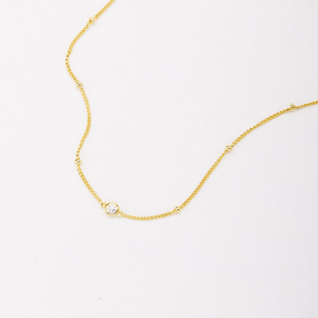 Close-up of a gold-tone bracelet showing a round bezel-set stone and small beads along the chain.