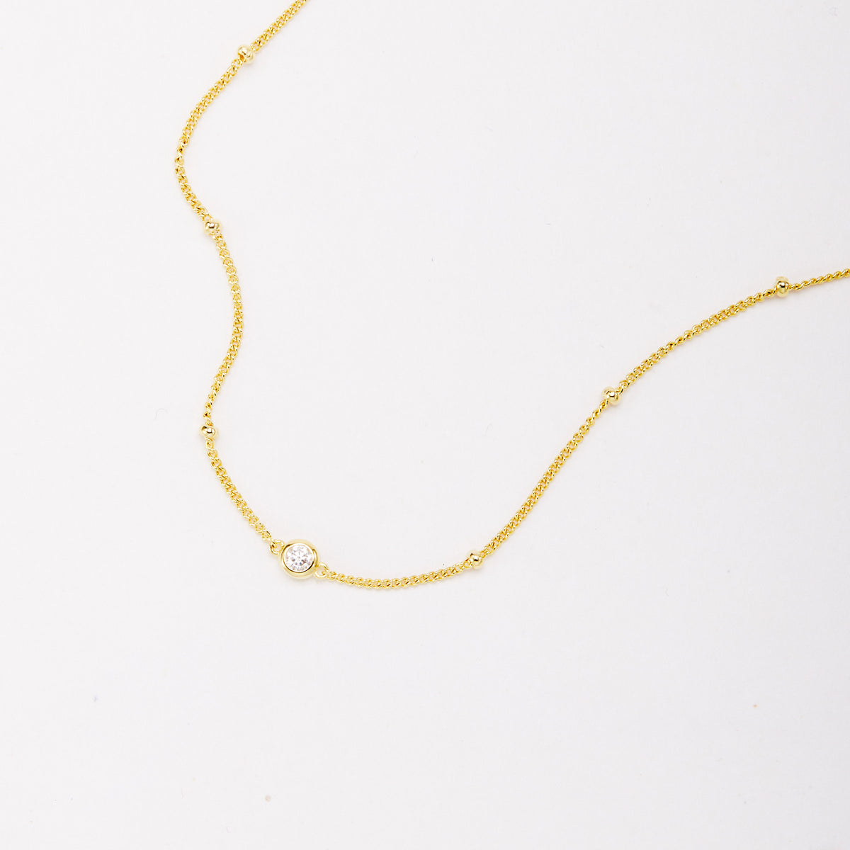 Close-up of a gold-tone bracelet showing a round bezel-set stone and small beads along the chain.
