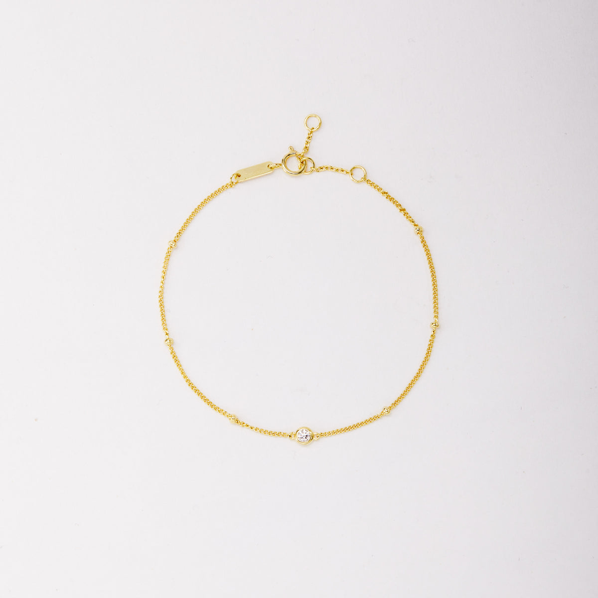 Gold-tone chain bracelet with small beads and a single round bezel-set stone, shown laid flat on a light background. Hauptbild