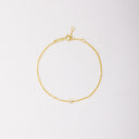 Gold-tone chain bracelet with small beads and a single round bezel-set stone, shown laid flat on a light background.