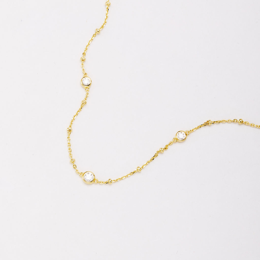 Close-up of three round bezel-set stones and small beads along a gold-tone chain bracelet.