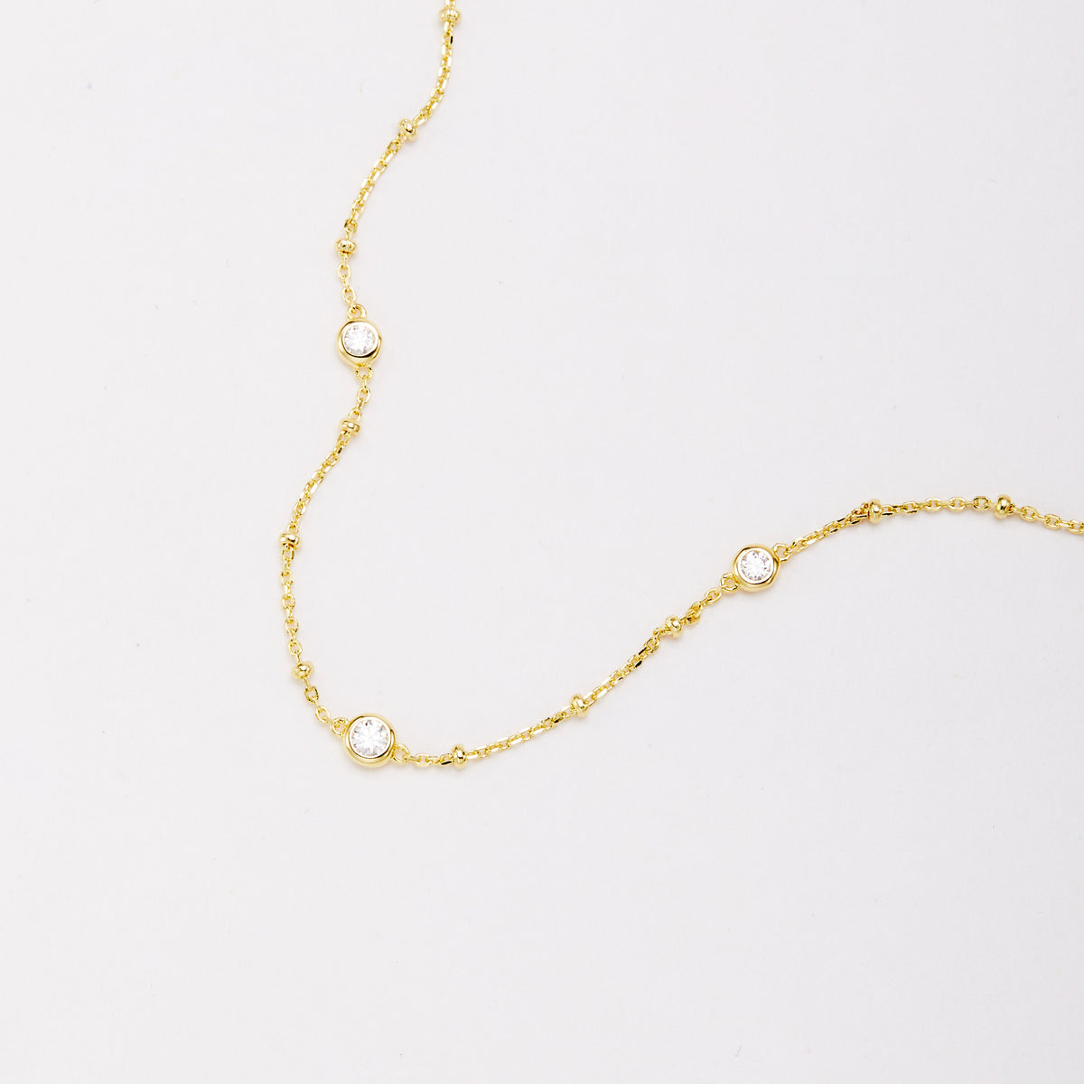 Close-up of three round bezel-set stones and small beads along a gold-tone chain bracelet.