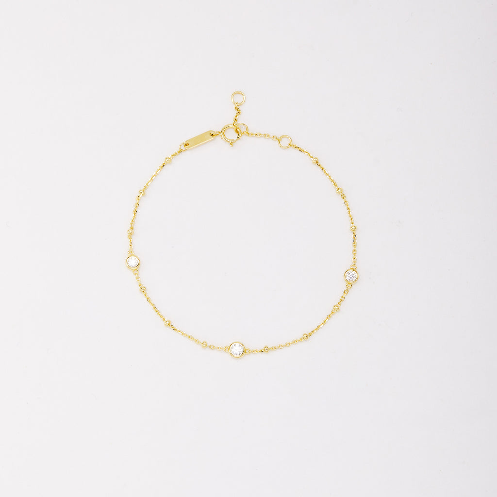 Gold-tone chain bracelet with three round bezel-set stones and small beads, shown laid flat on a light background.