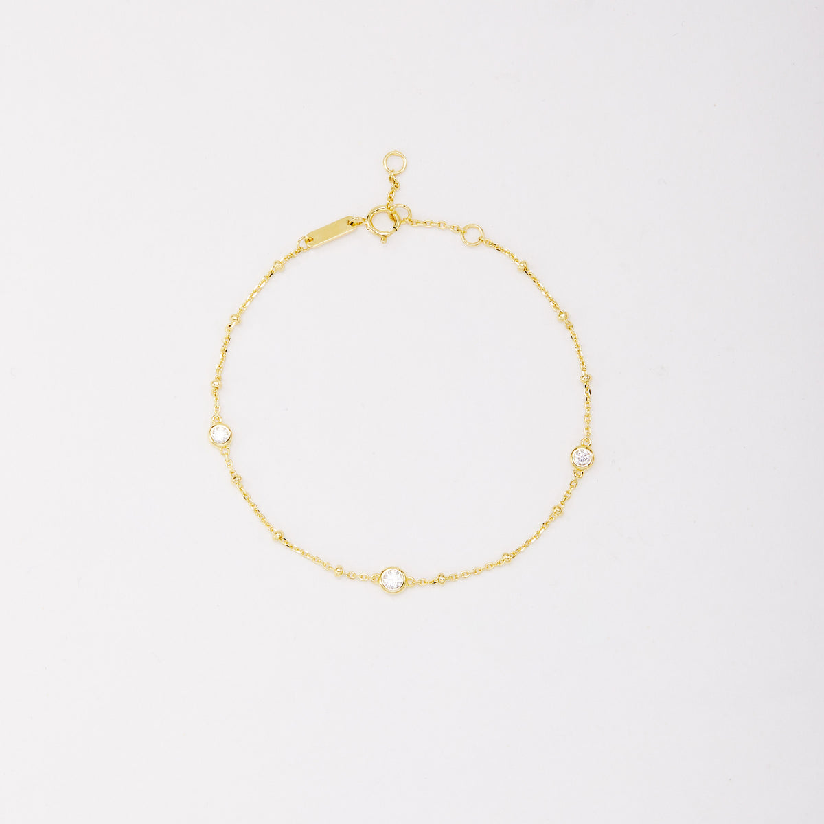 Gold-tone chain bracelet with three round bezel-set stones and small beads, shown laid flat on a light background.