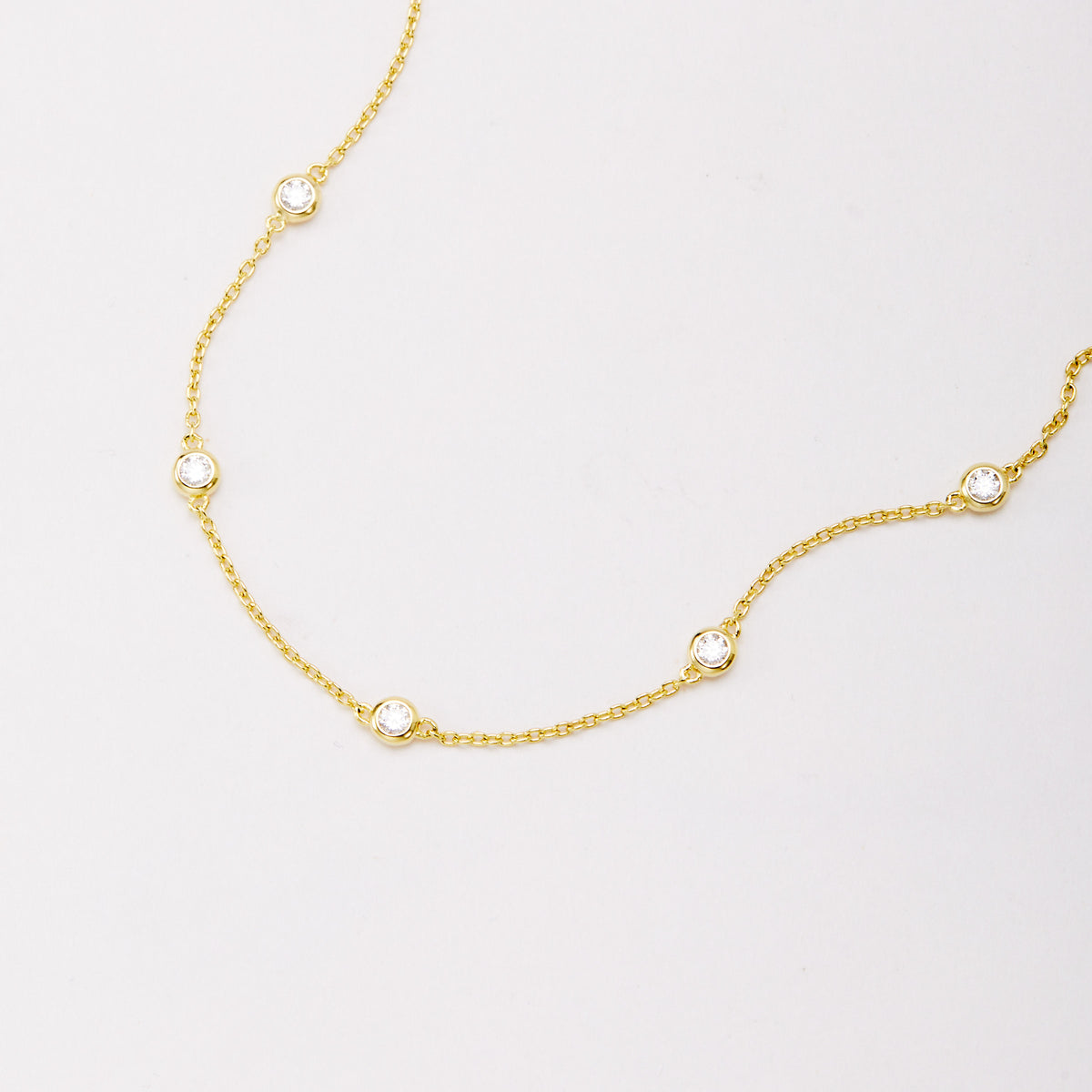 Close-up of five round bezel-set stones spaced along a gold-tone chain bracelet.