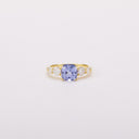 Front view of a gold-tone ring with a light blue cushion-shaped center stone and four clear side stones.