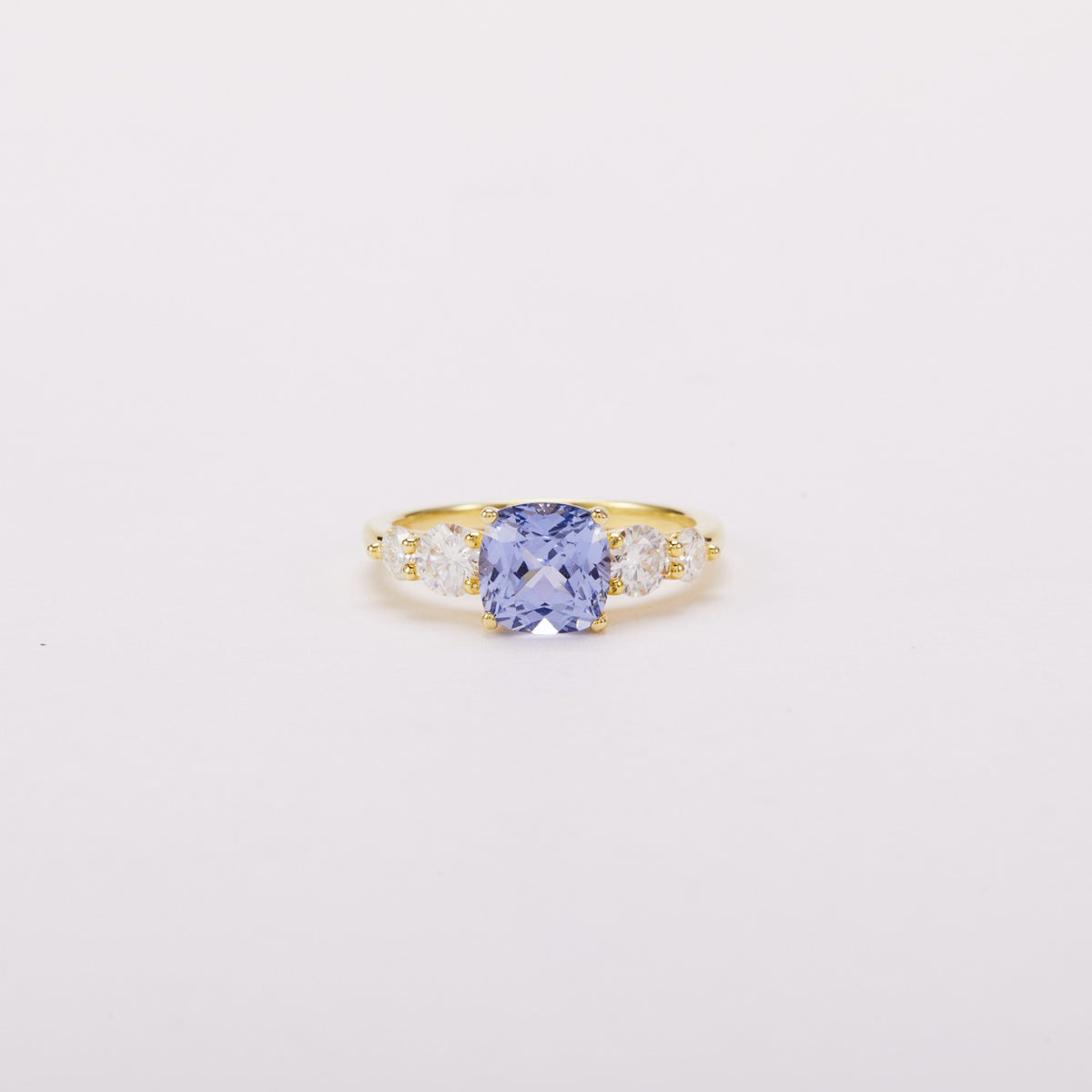 Front view of a gold-tone ring with a light blue cushion-shaped center stone and four clear side stones.